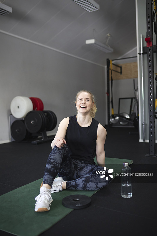 坐在健身房运动垫上的快乐年轻女人全身照图片素材