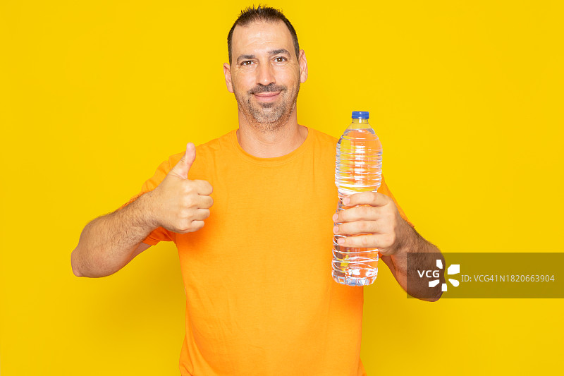 男人靠在黄色背景前手持水瓶肖像照图片素材