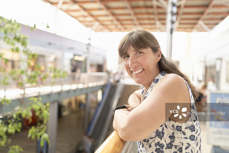 穿着休闲的女人靠在购物中心扶手上，看向街道远方的侧面视角图片素材