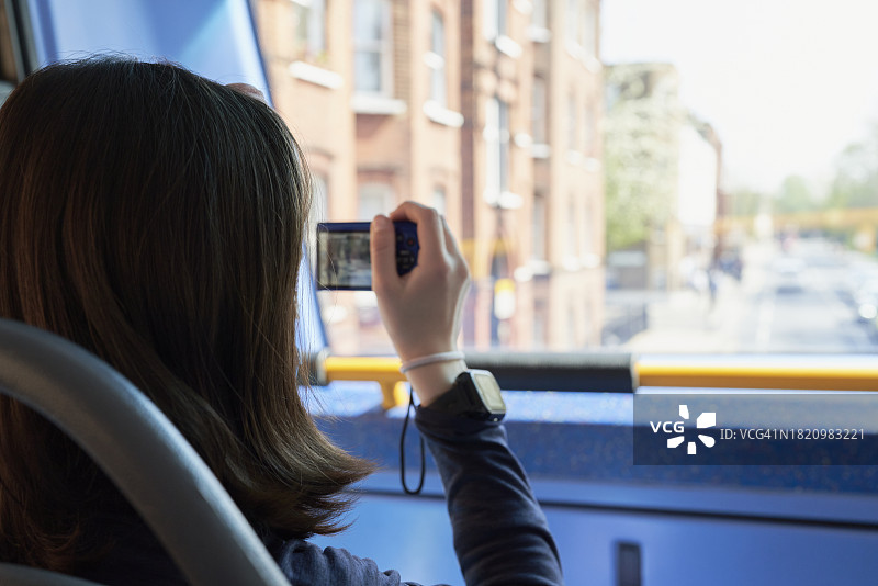 坐在旅游巴士上的棕发女孩手持数码相机看向前窗的背影图片素材