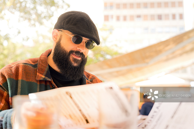 戴墨镜和贝雷帽的男人在城市露台上看菜单图片素材