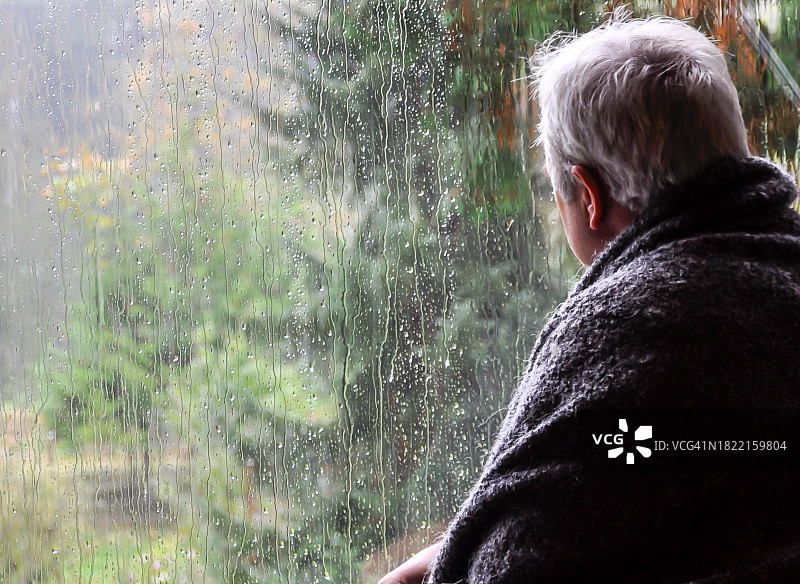 雨天，裹着毯子的男子在窗边向外看图片素材