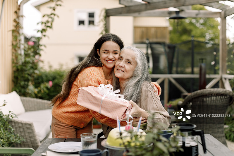 快乐的女孩在露台上拥抱奶奶并赠送生日礼物图片素材