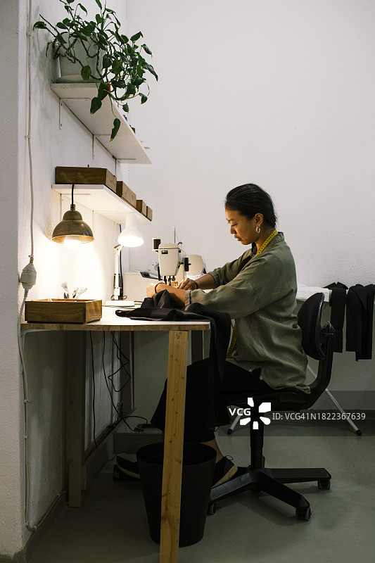 裁缝在工作室使用缝纫机缝制衣服的侧面图图片素材