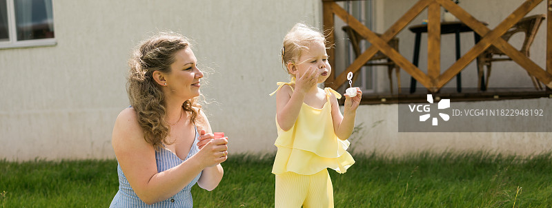 戴着人工耳蜗的小女孩和妈妈在户外玩耍，孩子吹着泡泡，有听力问题的孩子在手术后的适应。易拉宝，带文案空间图片素材