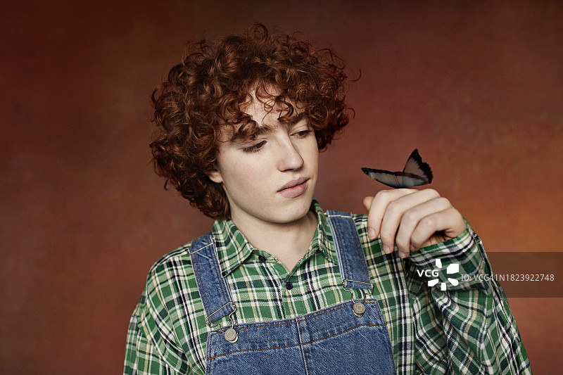 站在棕色背景前，手指上停着蝴蝶的青少年男孩图片素材