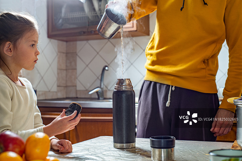 孩子和父亲在厨房里将热水倒入保温瓶图片素材