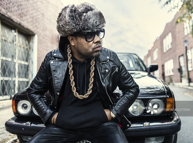 身穿复古嘻哈服装的男人站在老爷车前图片素材