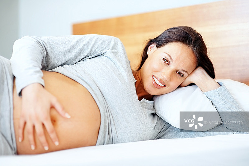 快乐的年轻孕妇在床上放松图片素材