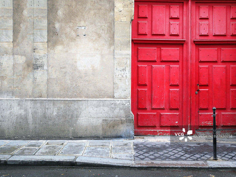 法国巴黎的旧红色门、风化的石墙、人行道和街道图片素材