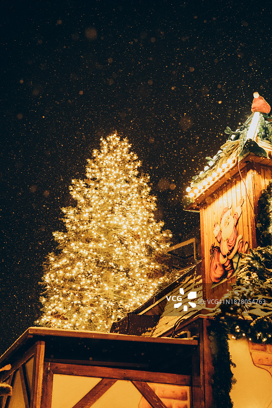 在下雪的夜晚，圣诞市场上装饰着灯光的节日圣诞冷杉树图片素材