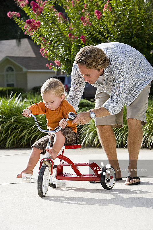 父亲帮助幼儿骑三轮车图片素材