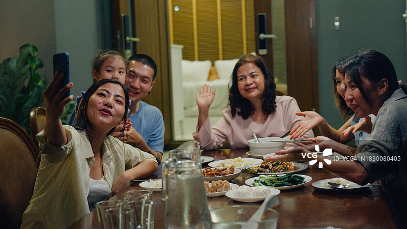 亚洲家庭使用手机视频通话，在后院餐桌旁愉快用餐。多代同堂共享美好时光图片素材