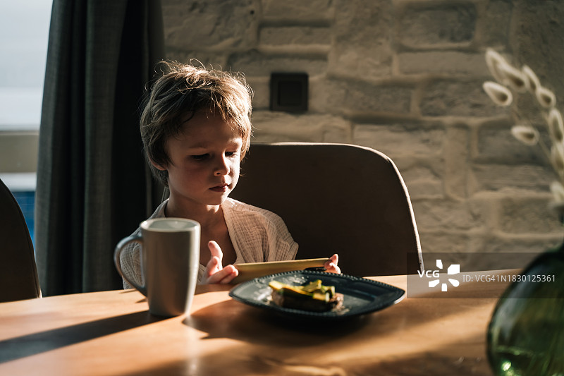 早晨在家，男孩坐在书桌前用智能手机看卡通片图片素材