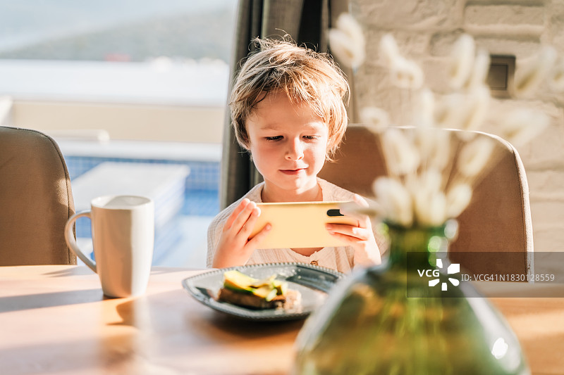 早晨在家，男孩坐在书桌前用智能手机看卡通片图片素材