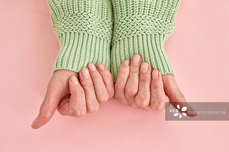 成年女性的手，裸色美甲，拿着粉色背景上的针织毛衣袖子图片素材