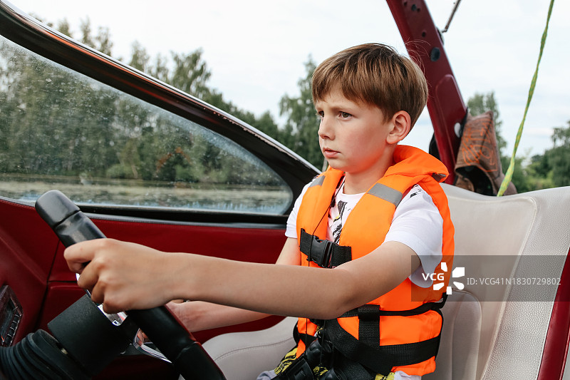 戴着橙色救生衣的严肃8-9岁男孩正在练习驾驶快艇图片素材