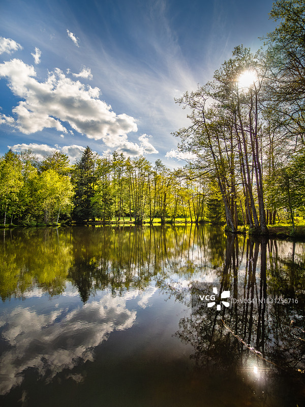法国东部，千塘高原地区池塘水中倒映的树木和云彩图片素材