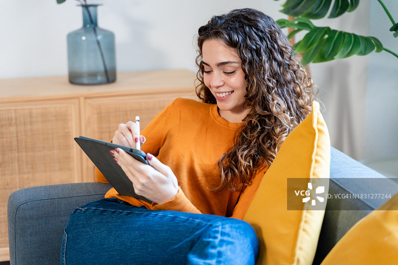 在家中沙发上使用平板电脑的微笑年轻女人图片素材
