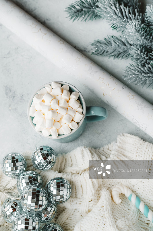 毛衣上放着一杯带有棉花糖、迪斯科花环和圣诞拐杖糖的马克杯，以及包装纸和冷杉树枝。图片素材