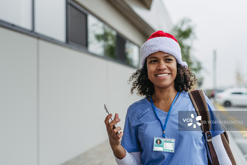 戴着圣诞帽的美丽的护士正在打电话。在圣诞节，圣诞节前夕在医院工作。图片素材