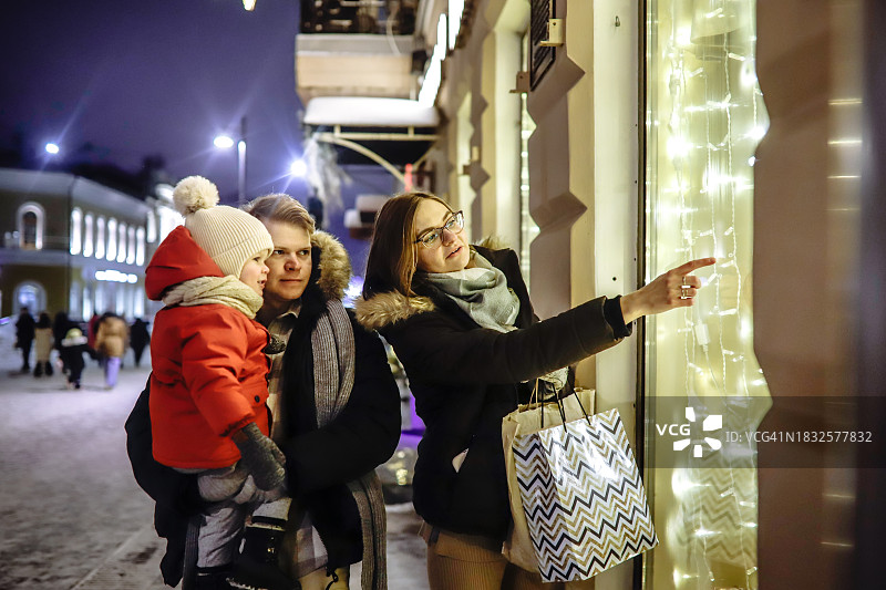 冬日城市之光：父母和幼儿欣赏圣诞橱窗夜景图片素材