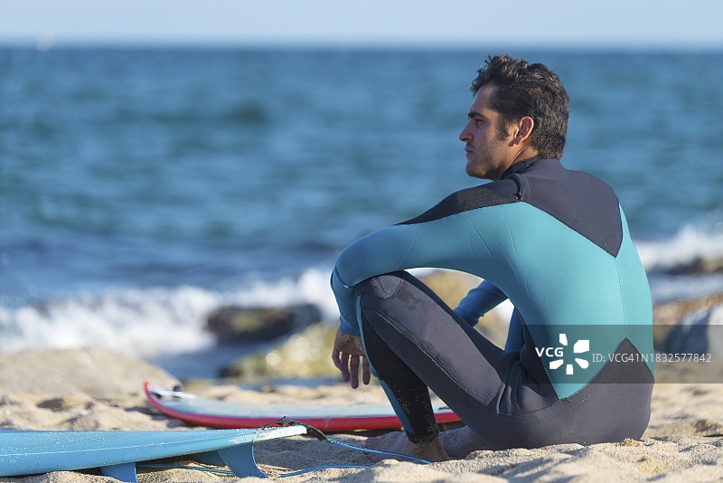 穿潜水服的男子坐在海滩上，看着大海图片素材