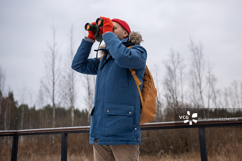 专注的男人在冬季森林里用双筒望远镜观鸟，在自然界中研究，爱好图片素材