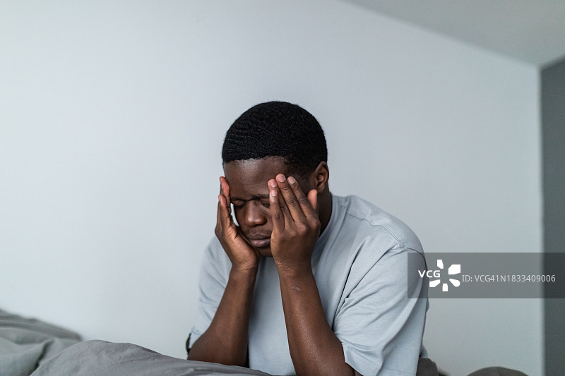 沮丧的年轻黑人男子坐在床上图片素材
