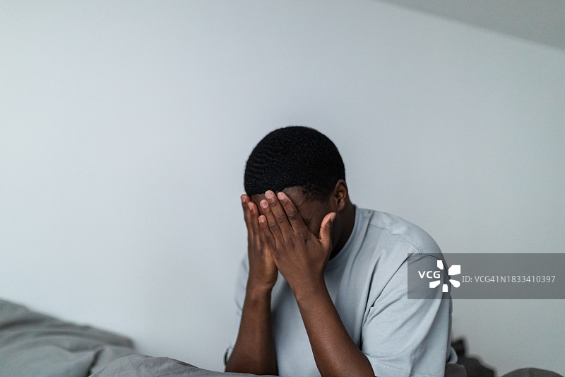 沮丧的年轻黑人男子坐在床上图片素材