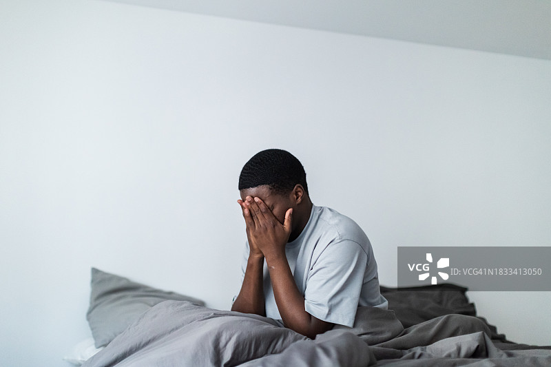 沮丧的年轻黑人男子坐在床上图片素材