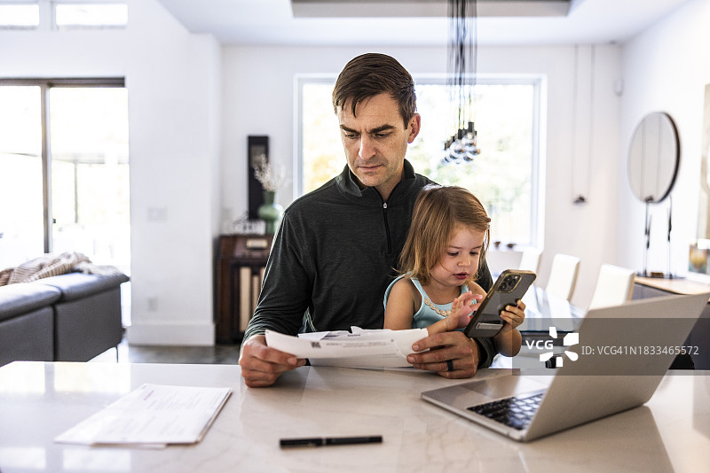父亲抱着蹒跚学步的女儿，在笔记本电脑上工作图片素材