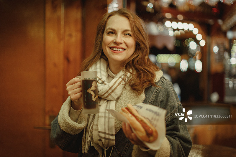 在圣诞市场喝热红酒、吃香肠的女人图片素材