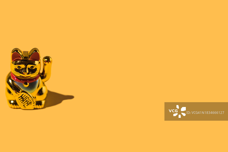 黄色背景下的金色招财猫：财富与好运的概念图片素材