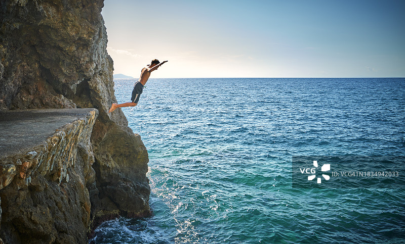 男孩从海边悬崖跳跃图片素材