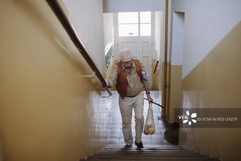 年长的男人提着一袋水果走上楼梯图片素材
