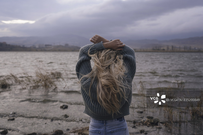 金发女人在日落时分张开双臂站在湖边图片素材