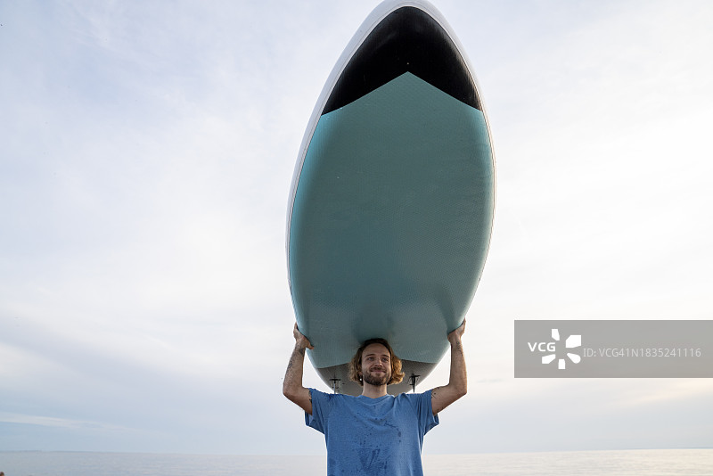 微笑的男子在日落时扛着桨板图片素材