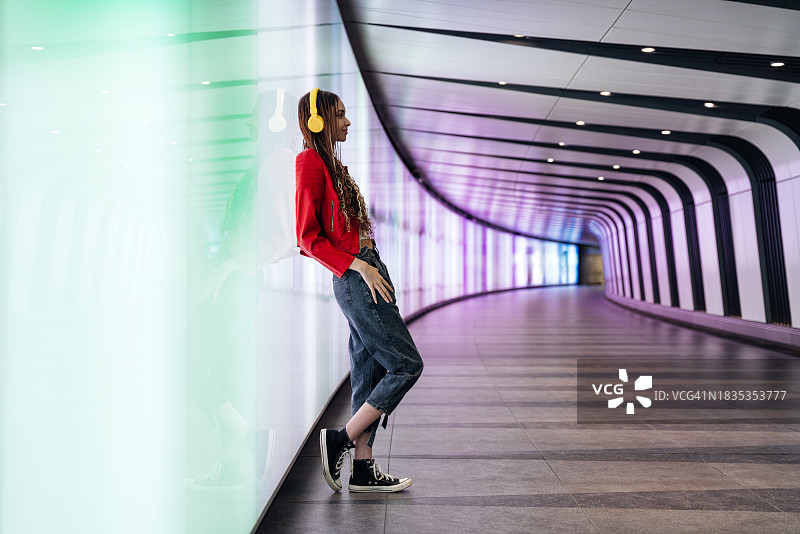戴着耳机靠在地下通道照明墙上的沉思女人图片素材