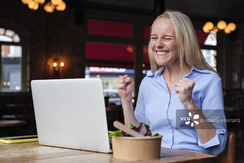 在酒吧里看笔记本电脑并欢呼的微笑的自由职业者图片素材