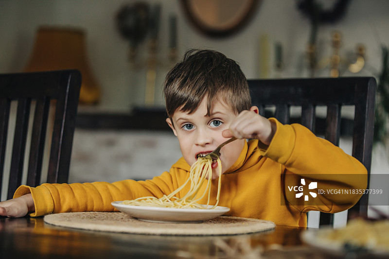 穿着连帽衫在家吃意大利面的男孩图片素材