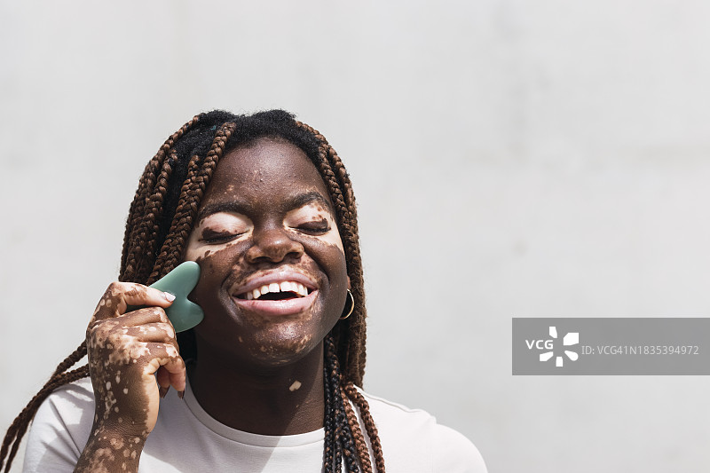 快乐的年轻女人在白墙前使用刮痧板图片素材