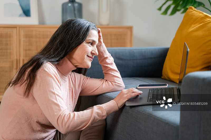在家坐在沙发上使用笔记本电脑的微笑老年女人图片素材