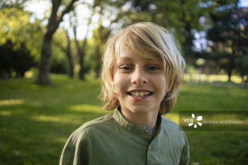 在公园树林前微笑的金发男孩图片素材