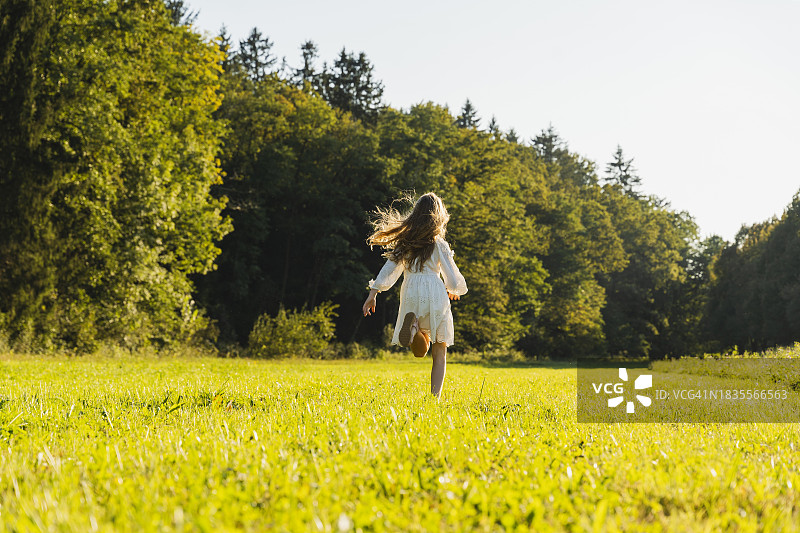 快乐女孩在草地上的树木前奔跑图片素材