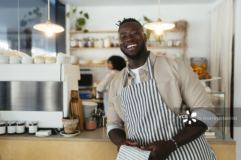 咖啡店里笑容满面的咖啡师，身穿围裙，手持毛巾图片素材