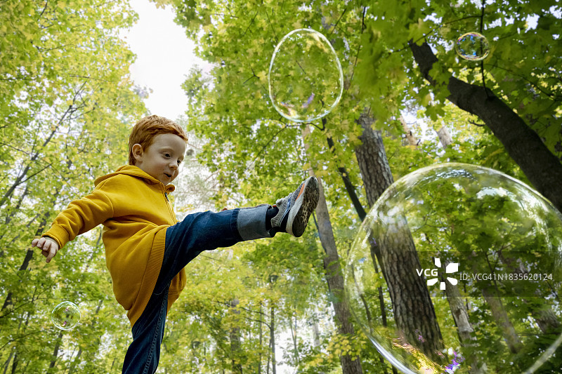 在秋季森林中踢肥皂泡的顽皮男孩图片素材