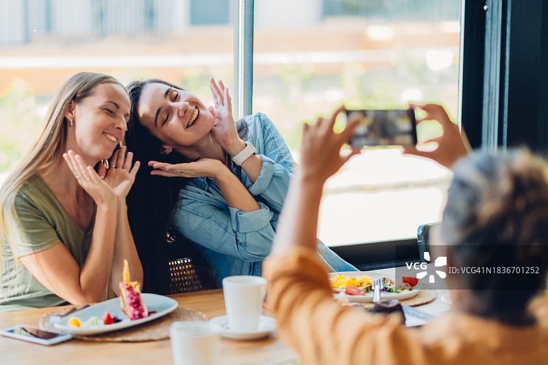 三位年轻漂亮的女性朋友在咖啡馆用手机拍照，共度美好时光。图片素材