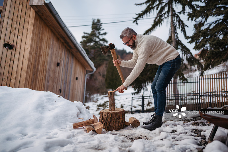 中年男人在小屋前砍柴，准备在壁炉和火炉中燃烧的柴火。英俊的男人在山间小屋度过轻松、无压力的冬季周末，享受独处时光。图片素材