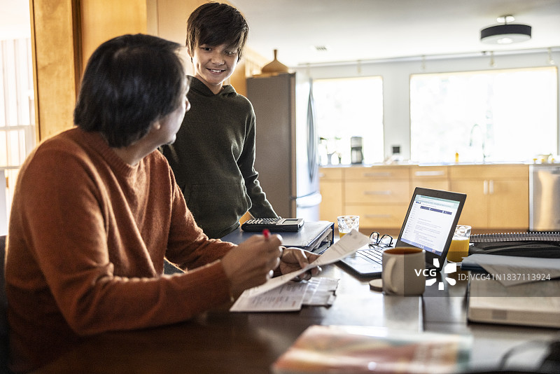 父亲在厨房的餐桌上使用笔记本电脑并支付账单图片素材